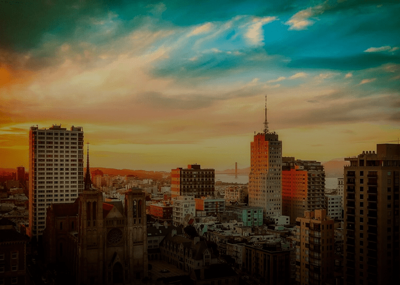 City skyline during a vibrant sunset with dramatic clouds.